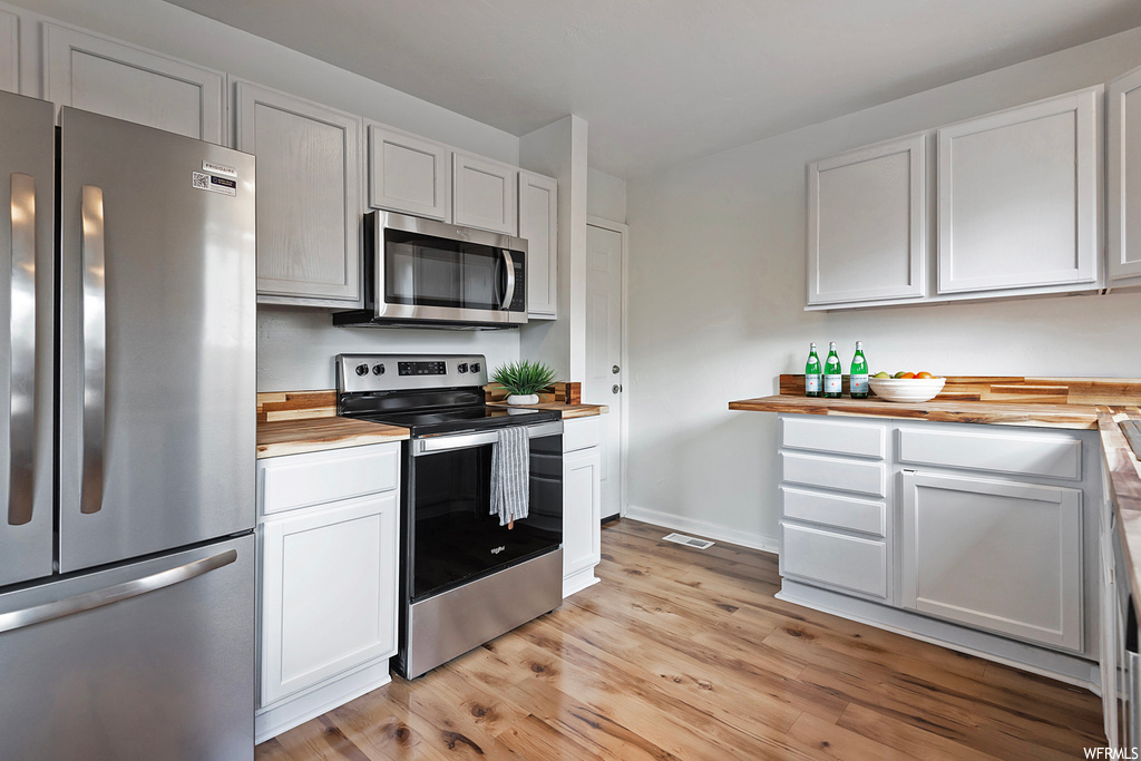 Kitchen featuring light hardwood flooring, stainless steel appliances, light countertops, and white cabinetry