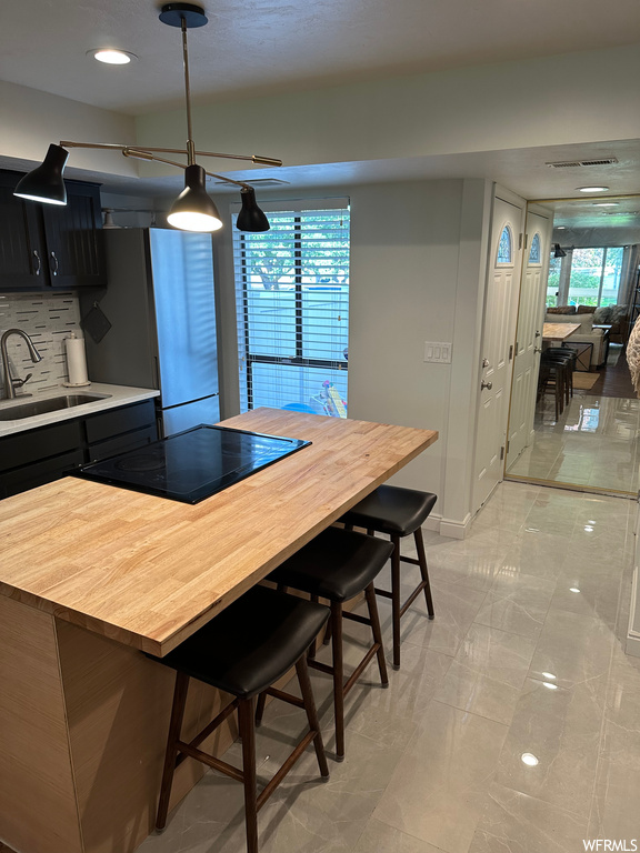 Kitchen with a kitchen island, decorative light fixtures, light tile flooring, light countertops, black electric stovetop, and backsplash