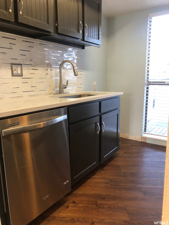 Kitchen featuring stainless steel dishwasher, backsplash, light countertops, dark brown cabinetry, and dark hardwood flooring