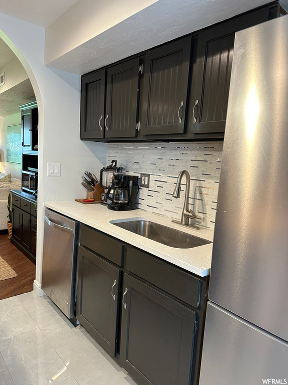 Kitchen with stainless steel dishwasher, refrigerator, light countertops, dark brown cabinets, backsplash, and light tile floors