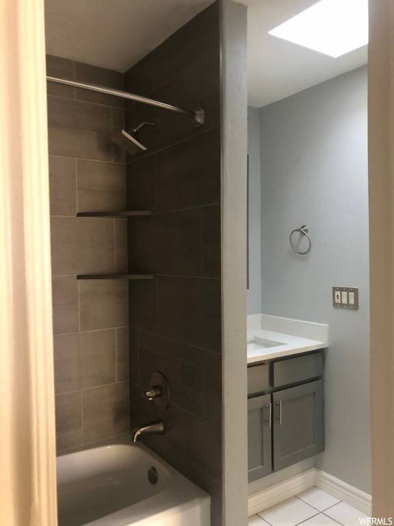 Bathroom with tiled shower / bath combo, light tile floors, and vanity