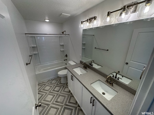 Full bathroom with dual large bowl vanity, a textured ceiling, light tile flooring, mirror, and tub / shower combination