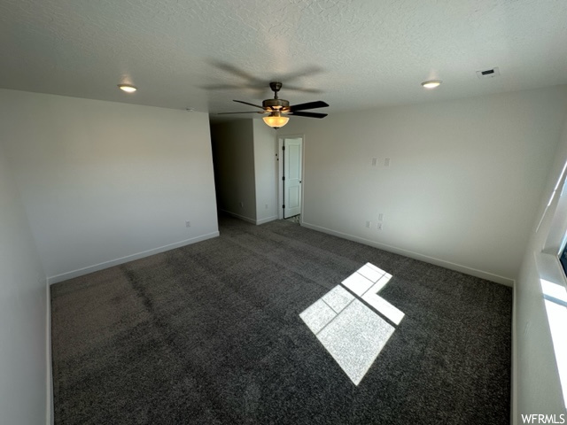 Spare room featuring dark carpet, a textured ceiling, and ceiling fan