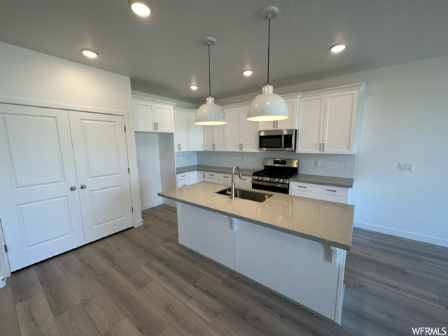 Kitchen featuring decorative light fixtures, backsplash, white cabinets, light countertops, appliances with stainless steel finishes, and hardwood floors