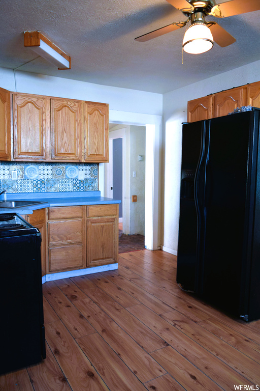 Kitchen with black appliances, brown cabinets, backsplash, light hardwood floors, and ceiling fan