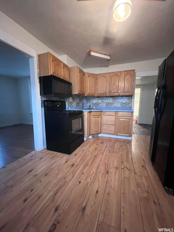 Kitchen with backsplash, brown cabinets, black appliances, and light hardwood flooring