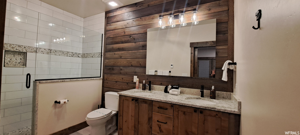 Bathroom featuring wood walls, a shower with door, double sink vanity, and mirror