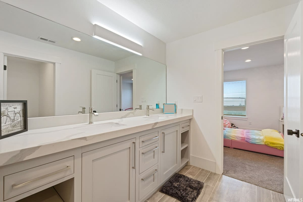 Bathroom with dual bowl vanity, mirror, and light hardwood floors