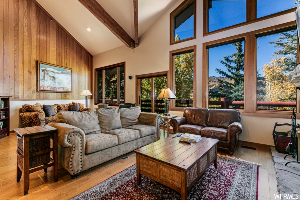 Living room featuring wood walls, beam ceiling, light hardwood floors, and vaulted ceiling high