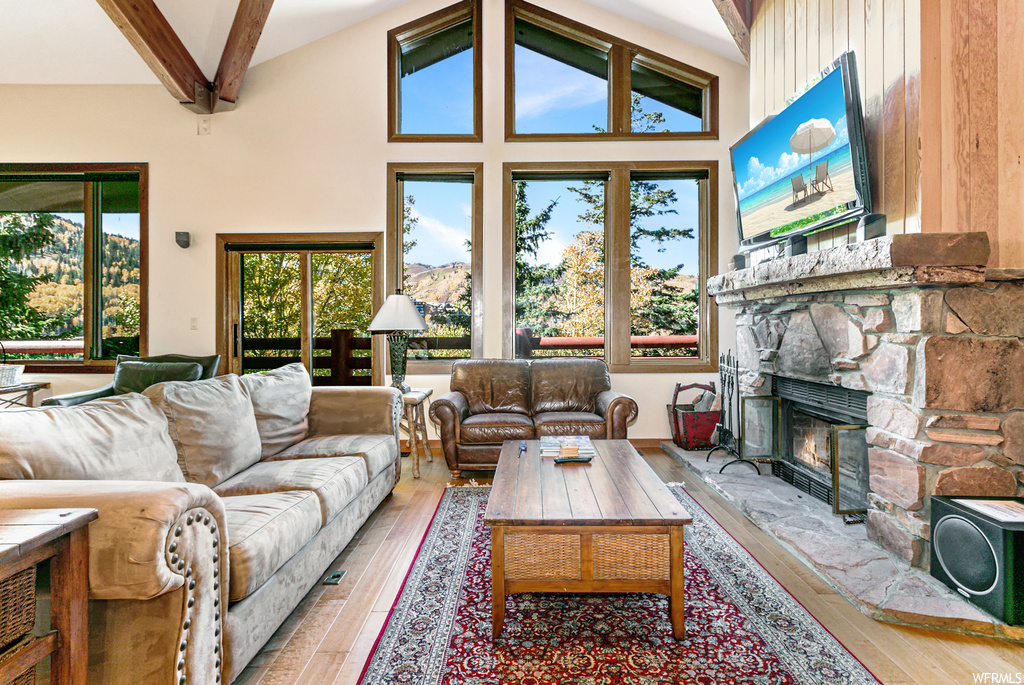 Living room featuring high vaulted ceiling, beam ceiling, a stone fireplace, and hardwood / wood-style floors