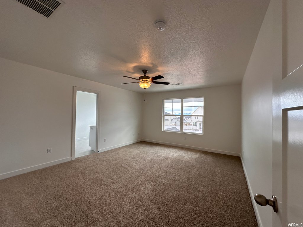 Carpeted spare room featuring ceiling fan and a textured ceiling