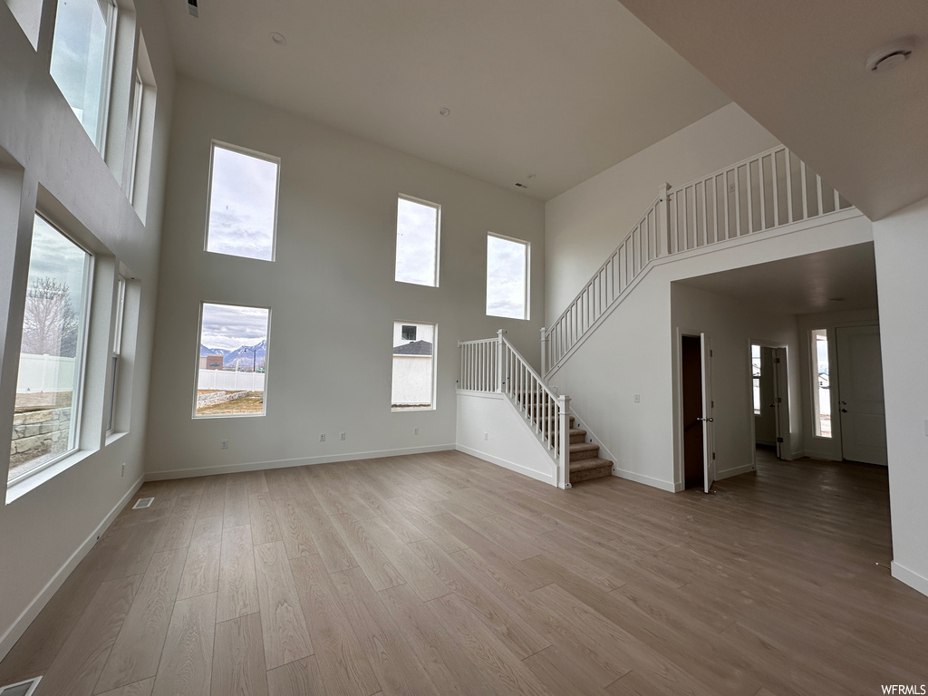 Empty room with a healthy amount of sunlight, a towering ceiling, and light hardwood / wood-style floors