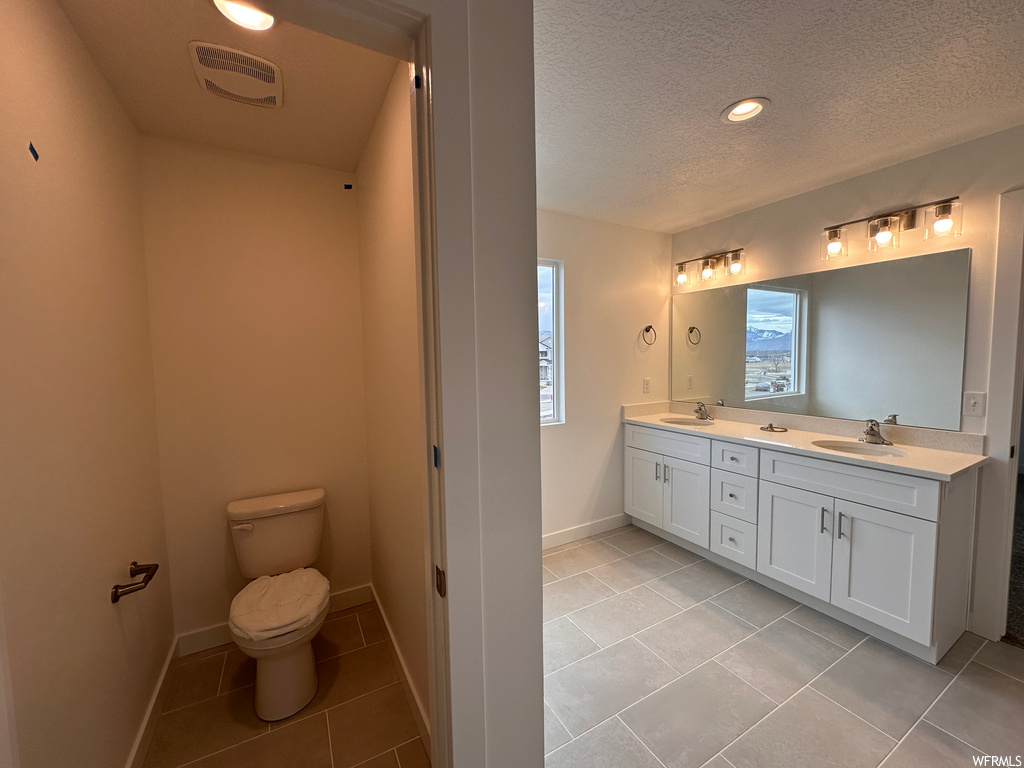 Bathroom with toilet, tile floors, a healthy amount of sunlight, and dual bowl vanity