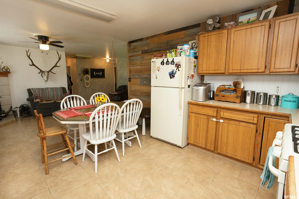 Kitchen with white refrigerator, range, brown cabinets, ceiling fan, and light tile flooring