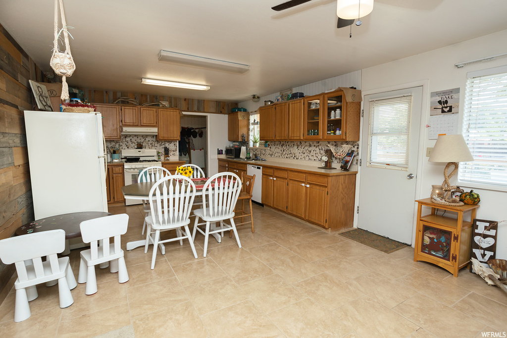 Kitchen featuring hanging light fixtures, backsplash, brown cabinets, light tile floors, ceiling fan, and white appliances