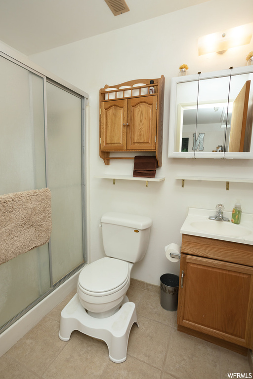 Bathroom featuring vanity, a shower with door, mirror, and light tile flooring