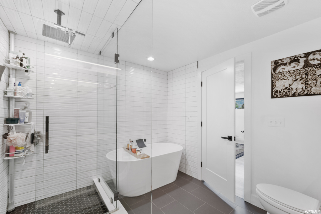 Bathroom featuring shower with separate bathtub, tile walls, and tile floors