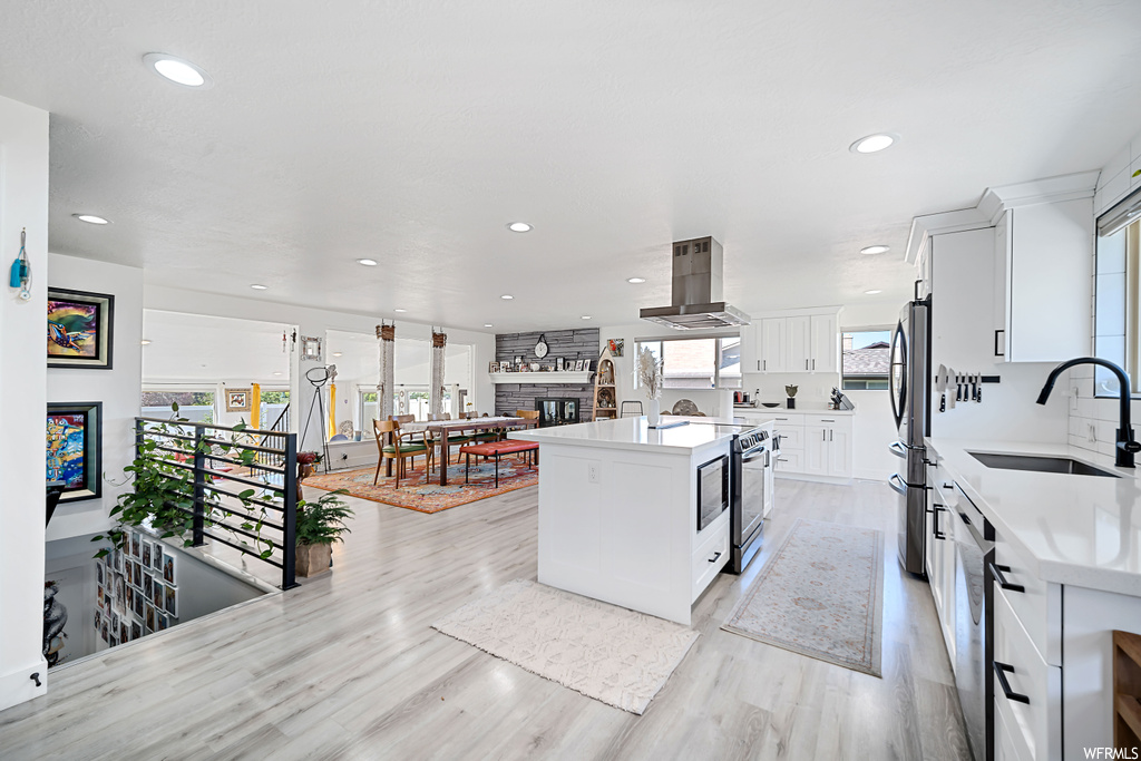 Kitchen featuring stainless steel appliances, a fireplace, light countertops, light hardwood flooring, and island exhaust hood