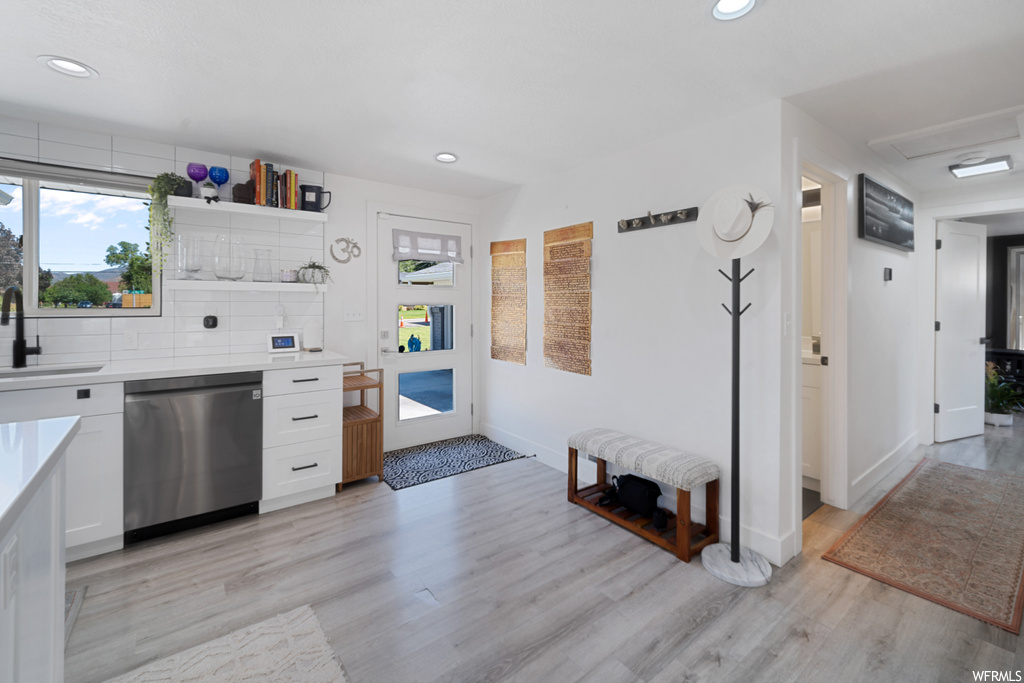 Kitchen with backsplash, stainless steel dishwasher, light hardwood floors, and light countertops