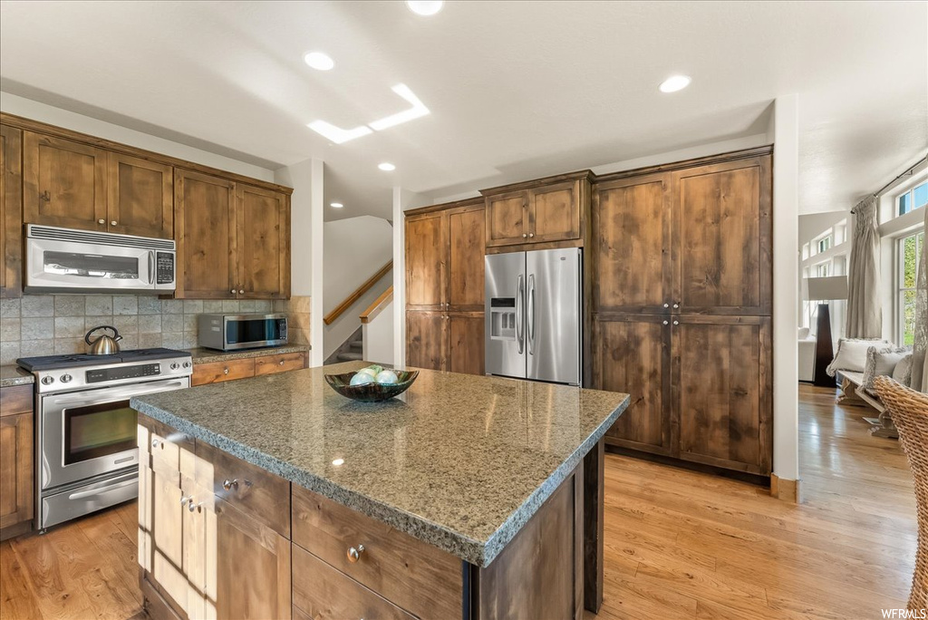 Kitchen featuring backsplash, brown cabinets, light hardwood floors, dark stone countertops, and stainless steel appliances