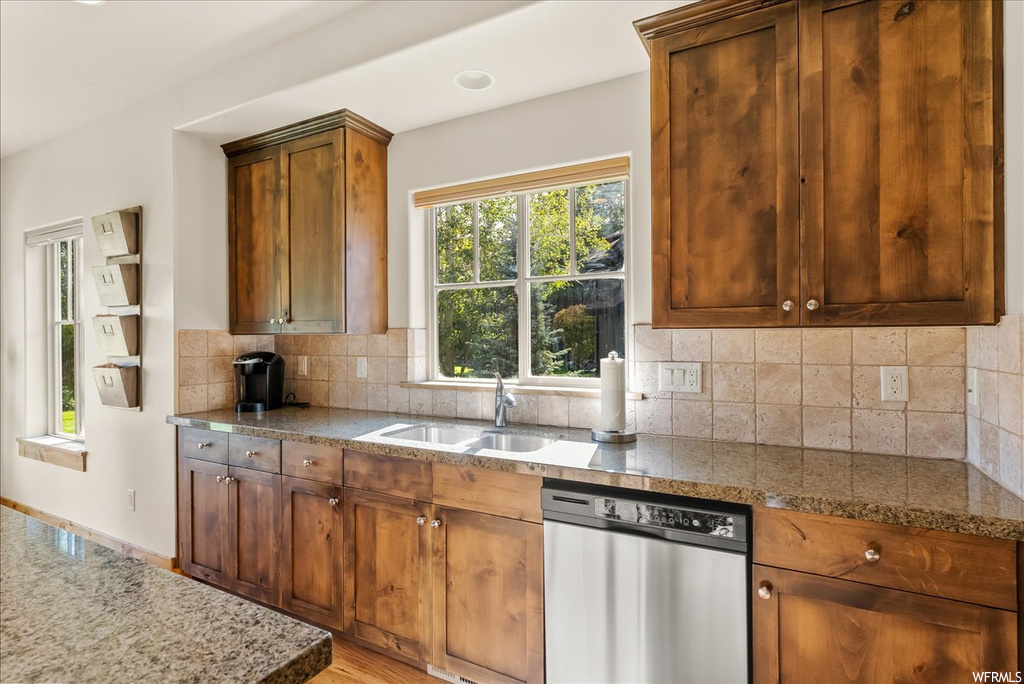 Kitchen with light hardwood flooring, stainless steel dishwasher, backsplash, and brown cabinets