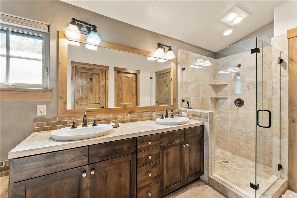 Bathroom with dual large bowl vanity, an enclosed shower, light tile flooring, mirror, vaulted ceiling, and backsplash