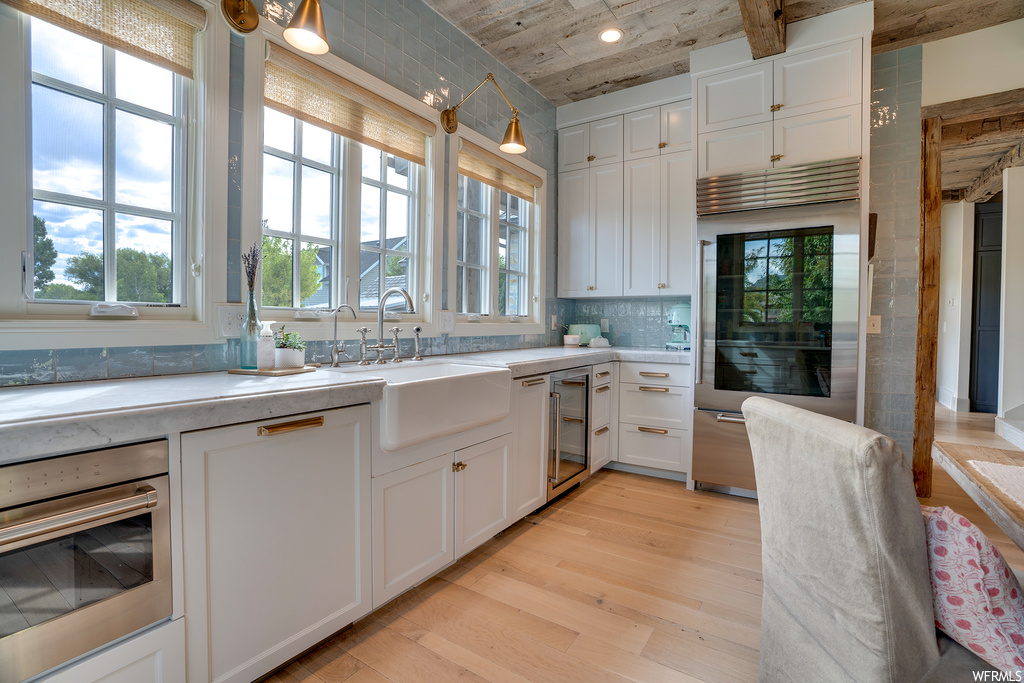 Kitchen featuring backsplash, white cabinets, light countertops, light hardwood flooring, and stainless steel appliances