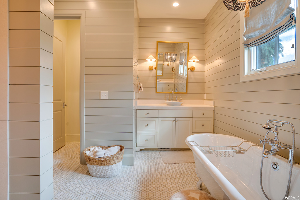 Bathroom with a washtub, mirror, wood walls, light tile floors, and vanity