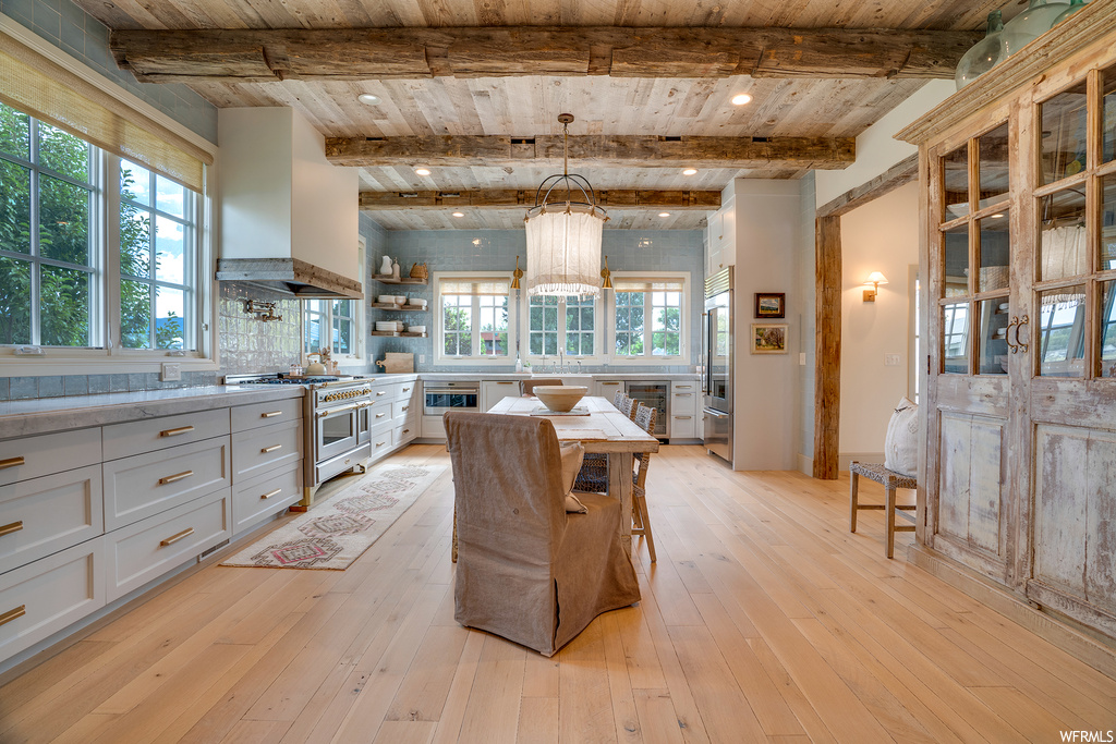 Kitchen featuring backsplash, beamed ceiling, light hardwood floors, custom exhaust hood, premium appliances, light stone countertops, and wood ceiling