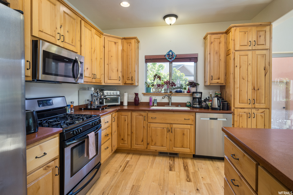 Kitchen featuring appliances with stainless steel finishes, dark countertops, light hardwood floors, and brown cabinets