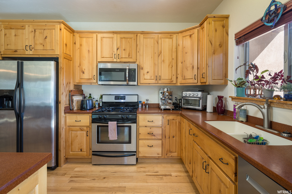 Kitchen with appliances with stainless steel finishes, dark countertops, light hardwood floors, and brown cabinets