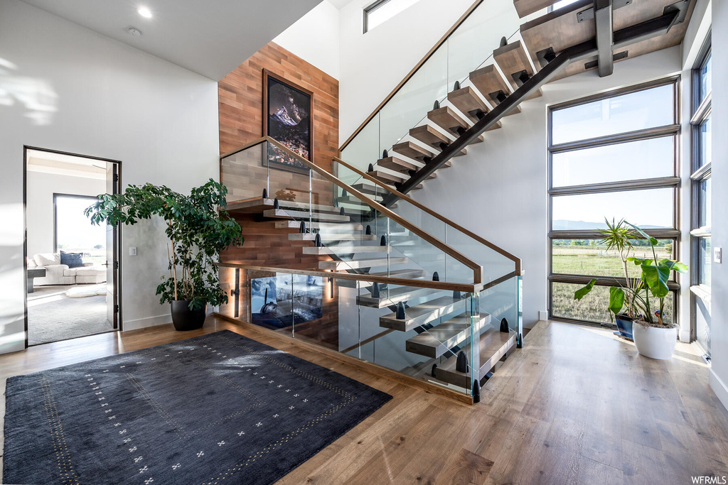 Stairs featuring wooden walls, a healthy amount of sunlight, a high ceiling, and light hardwood flooring