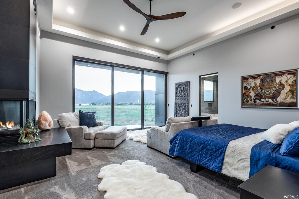 Bedroom with light carpet, a tray ceiling, a fireplace, and ceiling fan