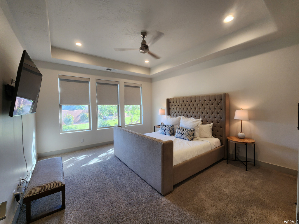 Bedroom featuring a tray ceiling, dark carpet, and ceiling fan