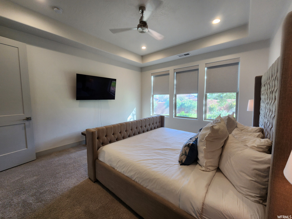 Bedroom featuring light carpet, a raised ceiling, and ceiling fan