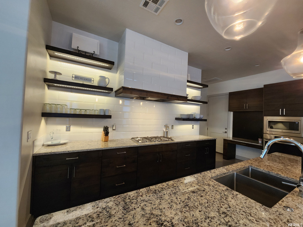 Kitchen featuring light stone counters, backsplash, stainless steel appliances, and dark brown cabinetry