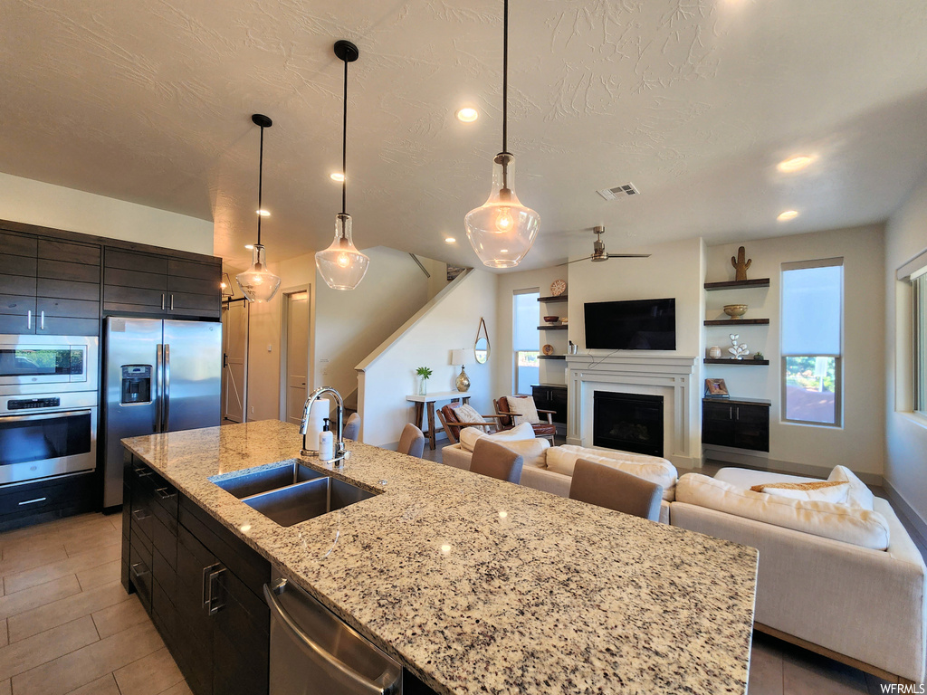 Kitchen featuring appliances with stainless steel finishes, plenty of natural light, decorative light fixtures, light tile flooring, a fireplace, and light stone countertops