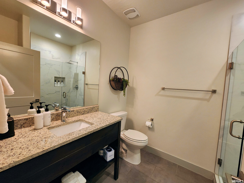 Bathroom with dark tile floors, vanity with extensive cabinet space, mirror, and a shower with door