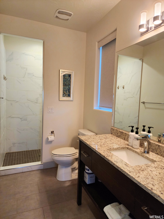 Bathroom featuring dark tile floors, vanity, mirror, and a tile shower
