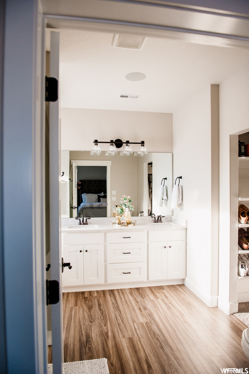 Bathroom with light hardwood flooring, dual vanity, and mirror