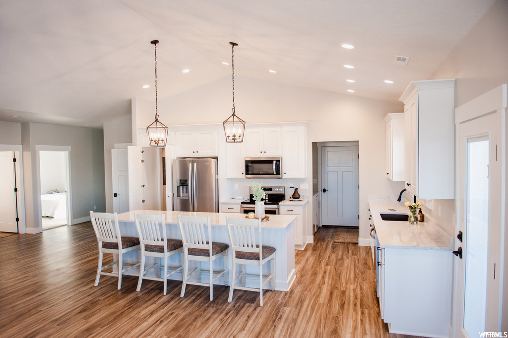 Kitchen featuring light hardwood floors, appliances with stainless steel finishes, a center island, lofted ceiling, pendant lighting, and a high ceiling