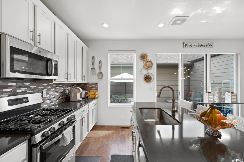 Kitchen with backsplash, light hardwood floors, white cabinetry, appliances with stainless steel finishes, dark stone countertops, and pendant lighting