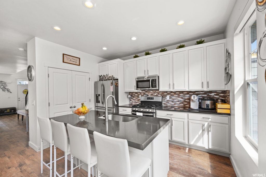 Kitchen with a kitchen island, white cabinetry, stainless steel appliances, dark countertops, light hardwood flooring, and backsplash