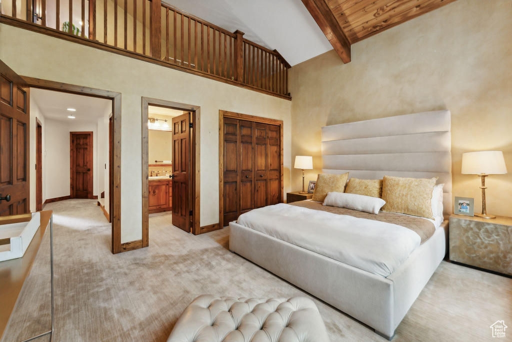 Carpeted bedroom with a closet, ensuite bath, high vaulted ceiling, beam ceiling, and wood ceiling