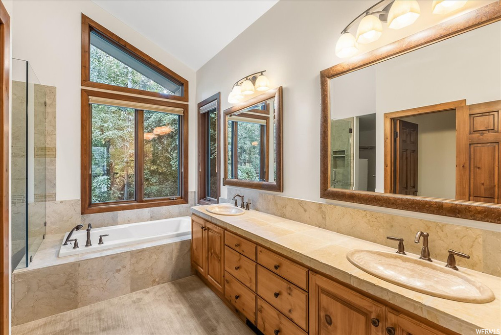 Bathroom with separate shower and tub enclosures, vaulted ceiling, double sink vanity, and mirror