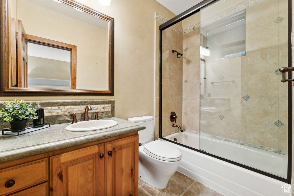 Full bathroom featuring bath / shower combo with glass door, toilet, vanity, tile patterned floors, and decorative backsplash