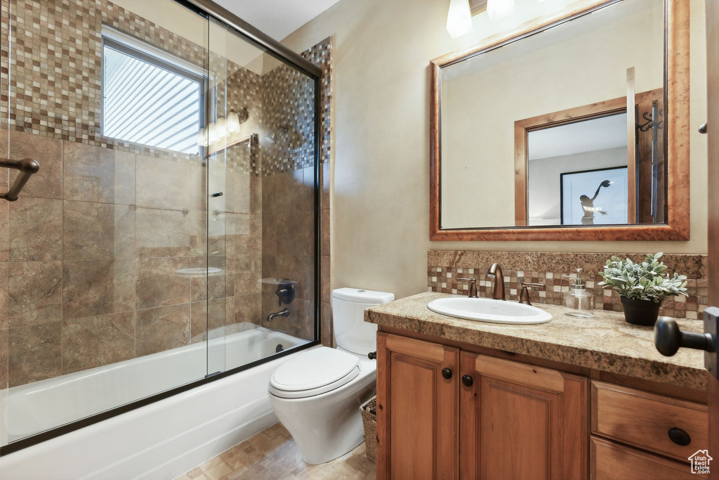 Full bathroom featuring vanity, toilet, combined bath / shower with glass door, and backsplash