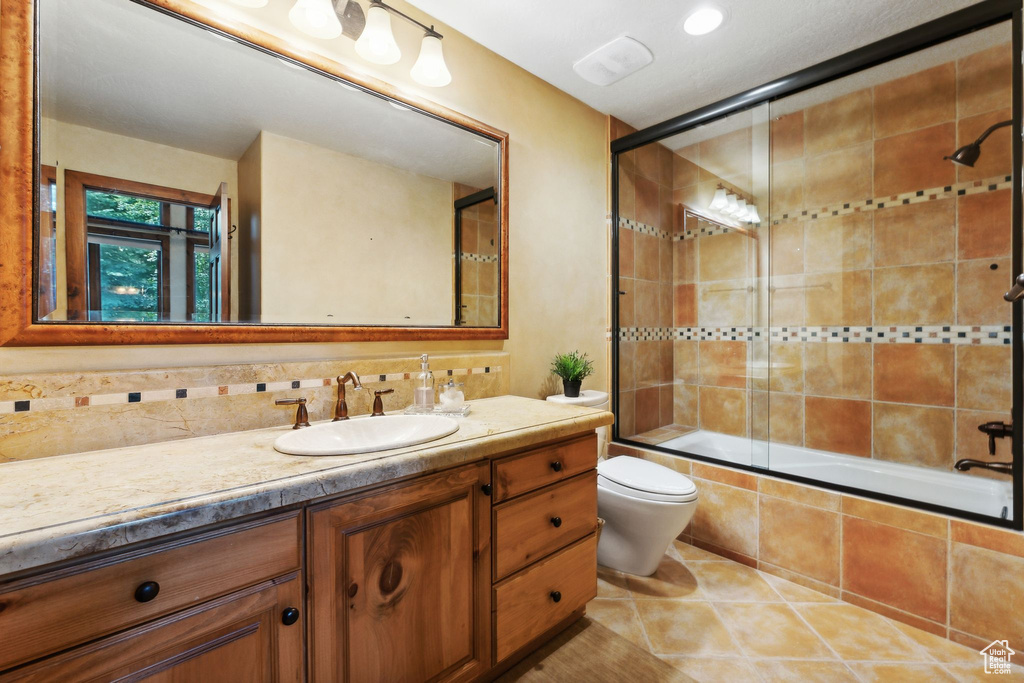 Full bathroom with shower / bath combination with glass door, backsplash, toilet, vanity, and tile patterned floors