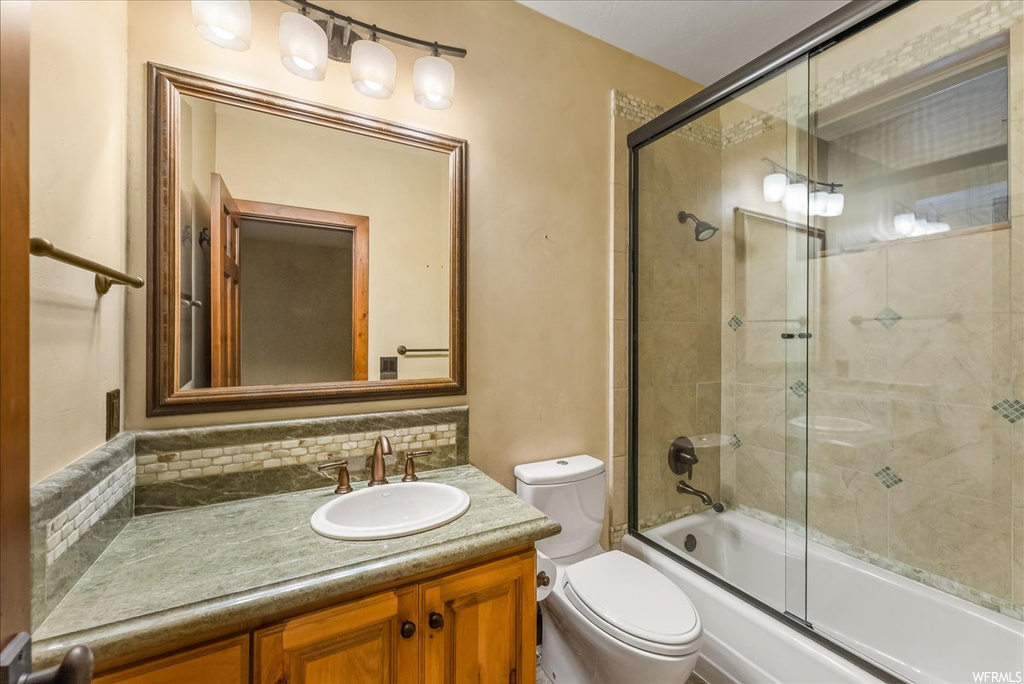 Full bathroom with backsplash, large vanity, bath / shower combo with glass door, and mirror