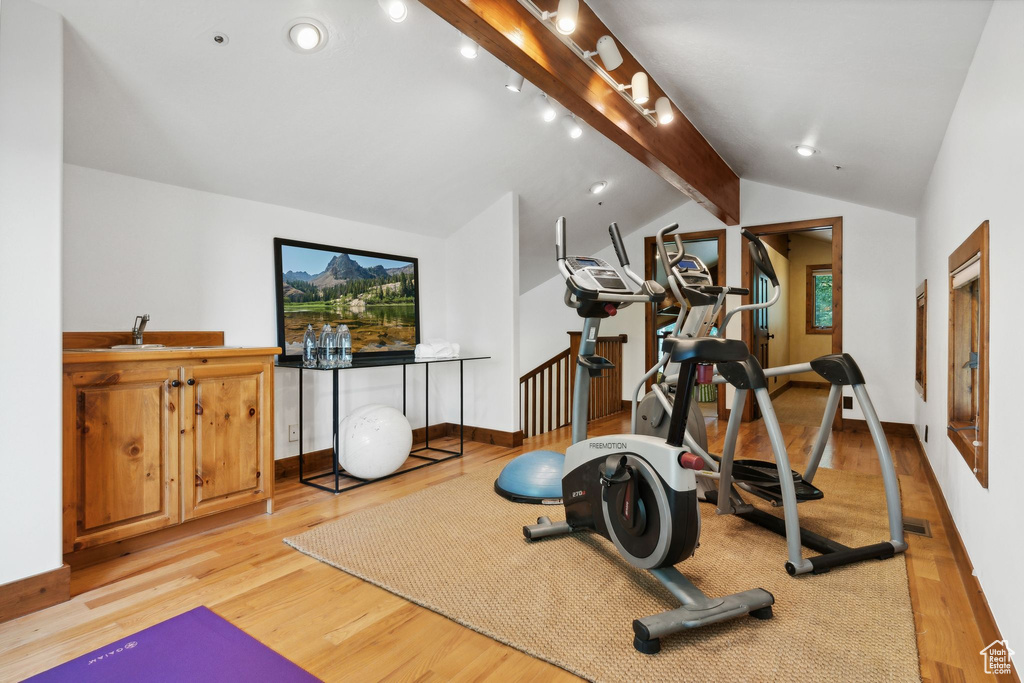 Workout room with light hardwood / wood-style floors, vaulted ceiling, track lighting, and sink